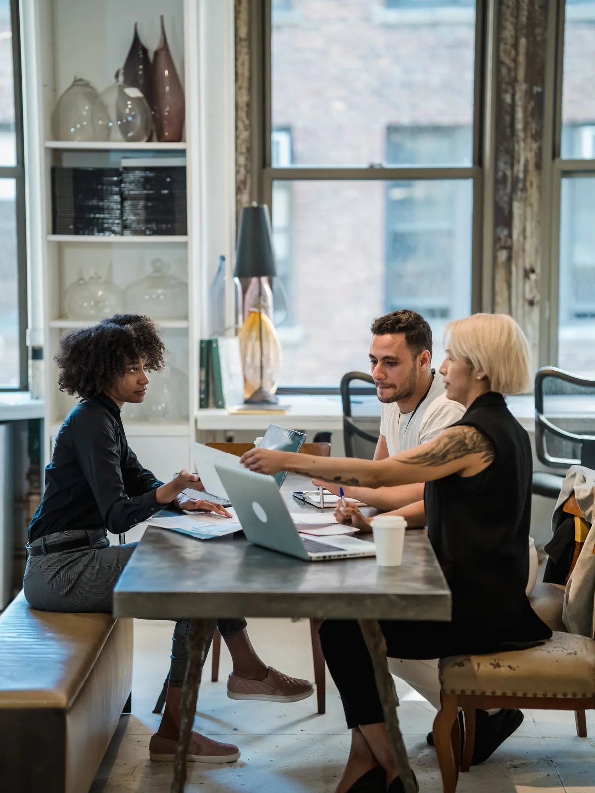 Colleagues discussing at a table by a large office window